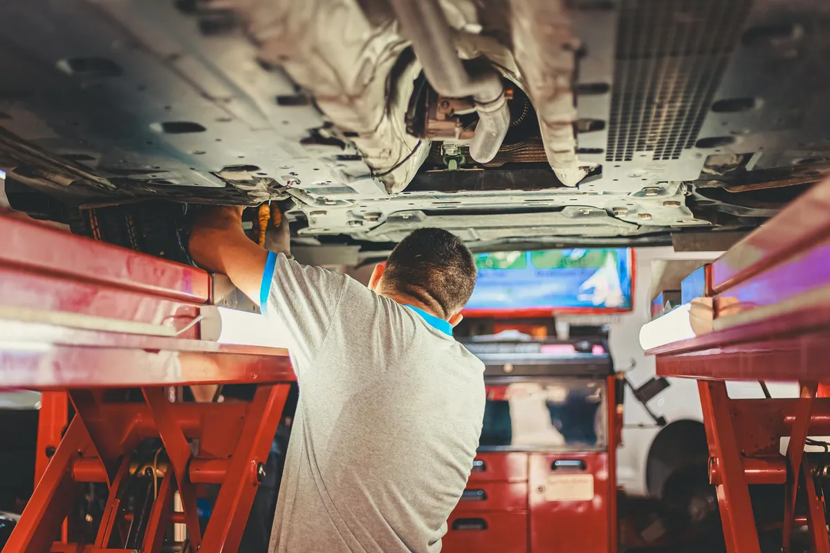 Mechanik pracuje pod podniesioną samochodem w warsztacie samochodowym, regulując części