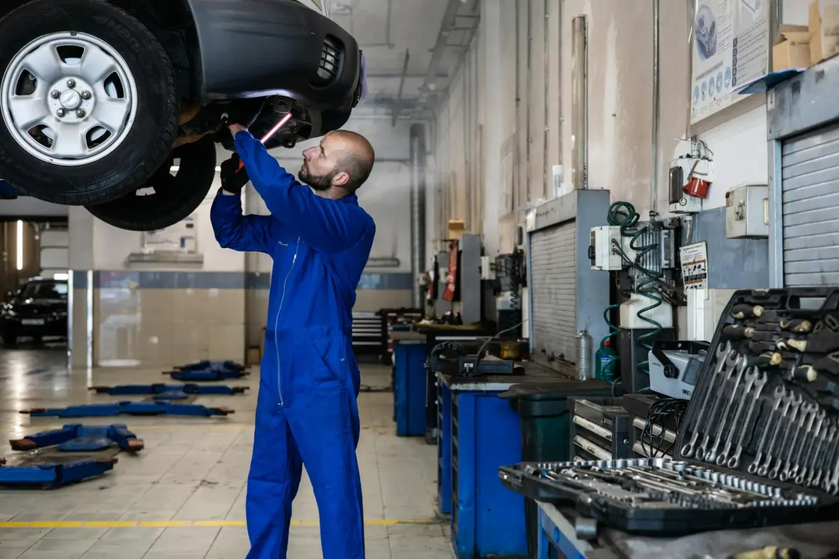Mechanik w niebieskim kombinezonie sprawdza podwozie samochodu uniesionego na podnośniku w warsztacie