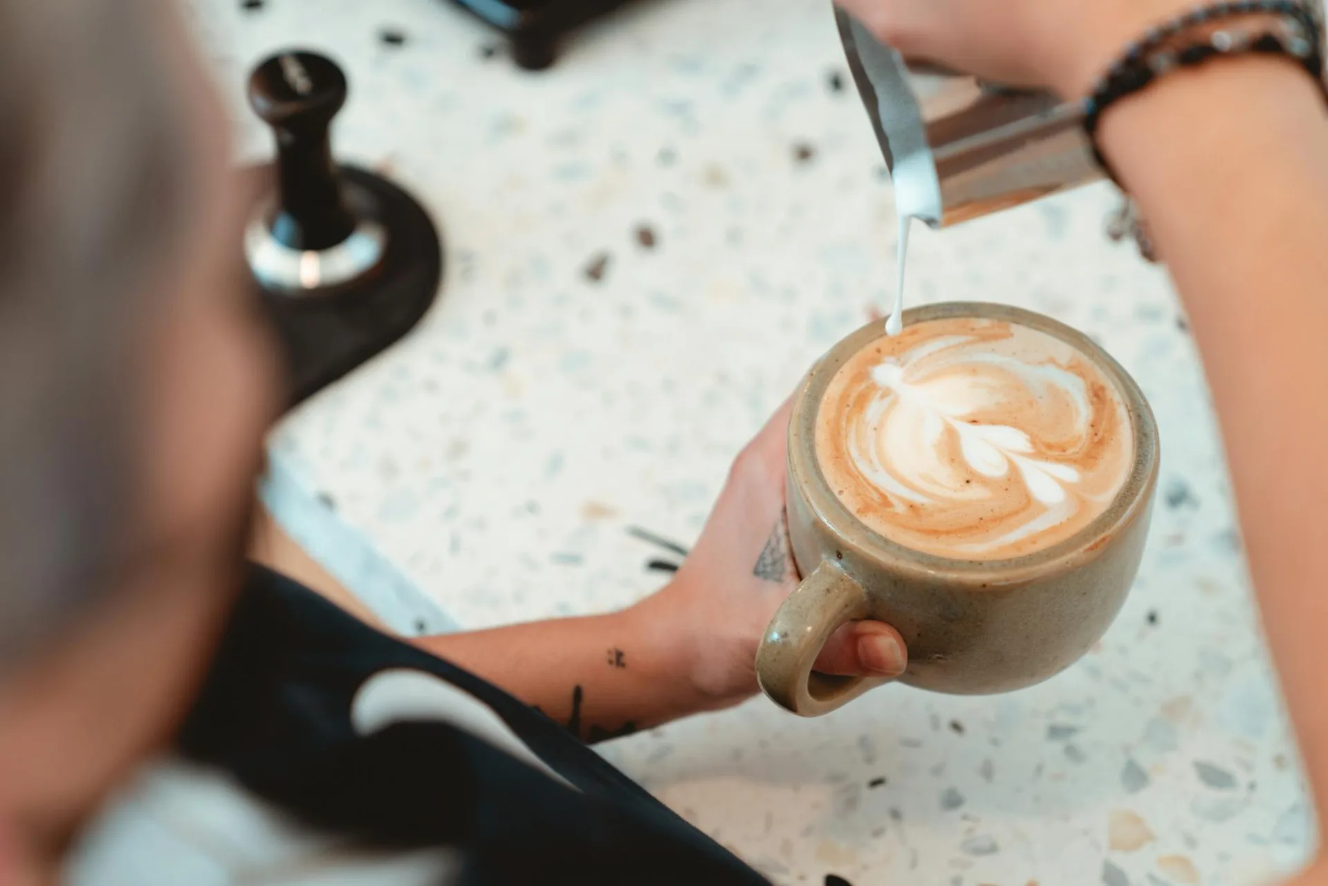 Barista tworząca skomplikowaną sztukę latte w przytulnym otoczeniu kawiarni, prezentując umiejętności i precyzję