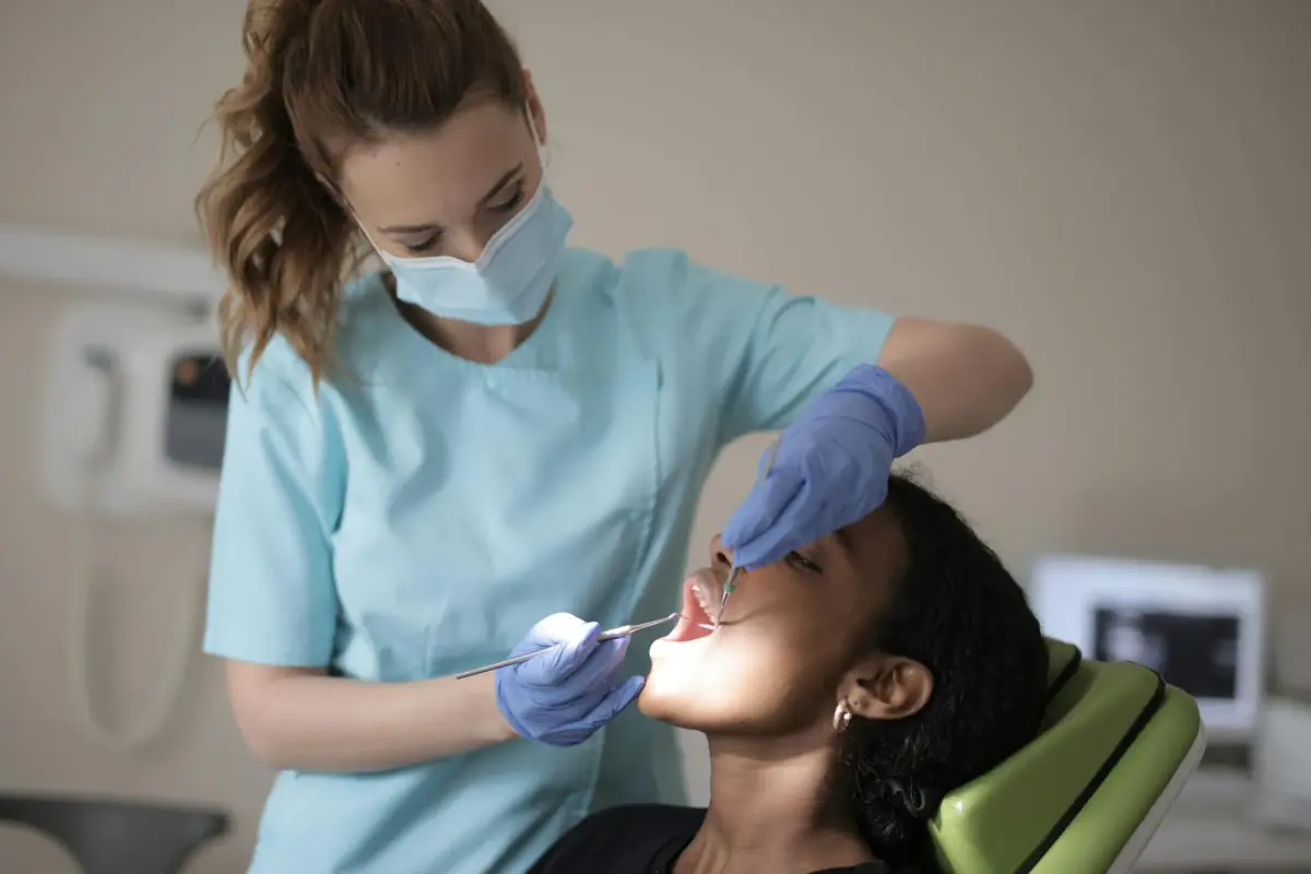 Lekarka dentystka w maseczce bada pacjentkę siedzącą na fotelu stomatologicznym