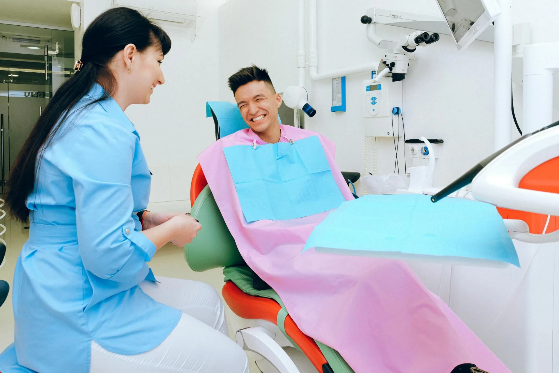 Szczęśliwy mężczyzna siedzi w fotelu dentystycznym i uśmiecha się rozmawiając z dentystką w mundurze przed leczeniem w nowoczesnej klinice