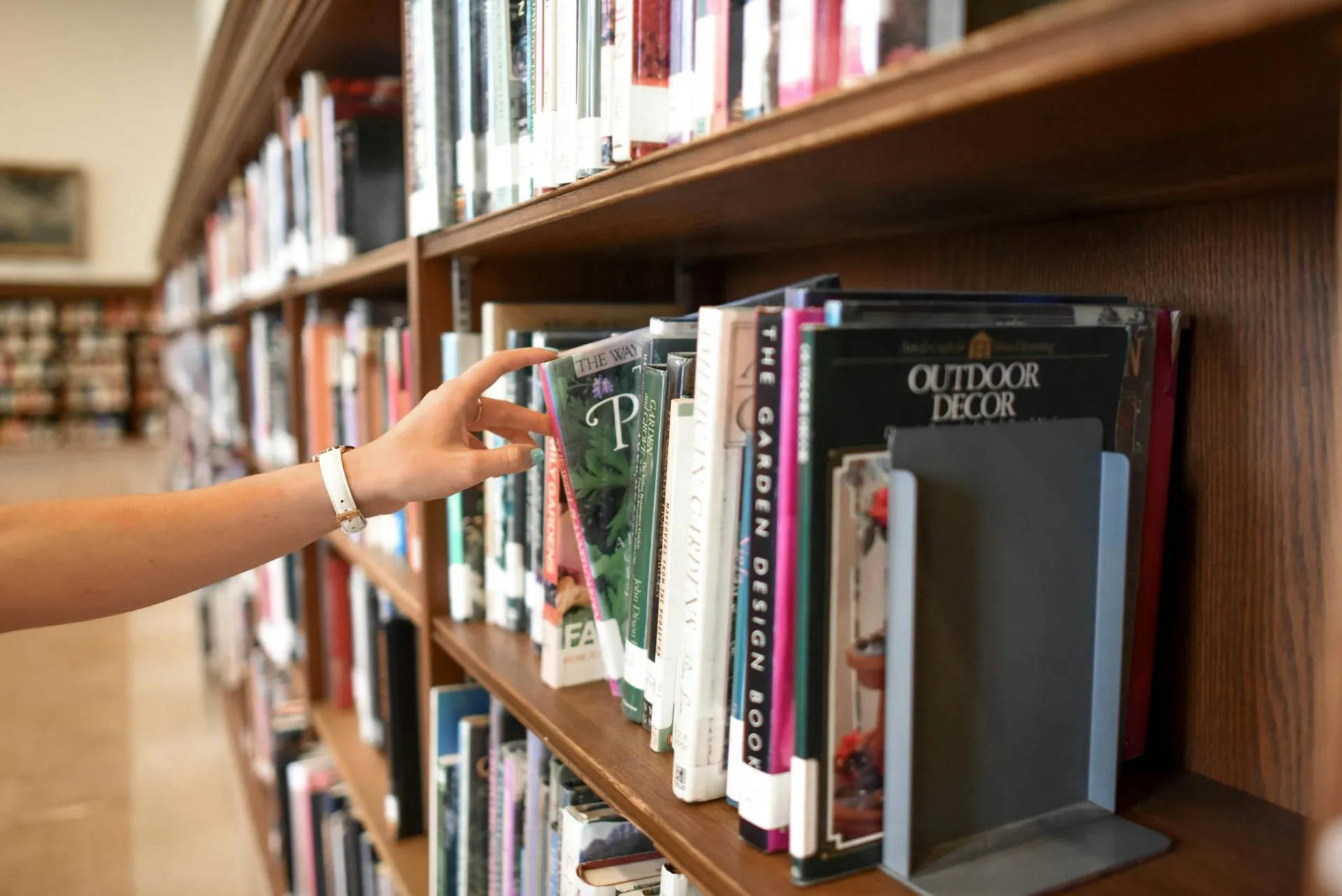 Zbliżenie: ręka sięgająca po książkę w bibliotecznym regale, sugerujące eksplorację i naukę